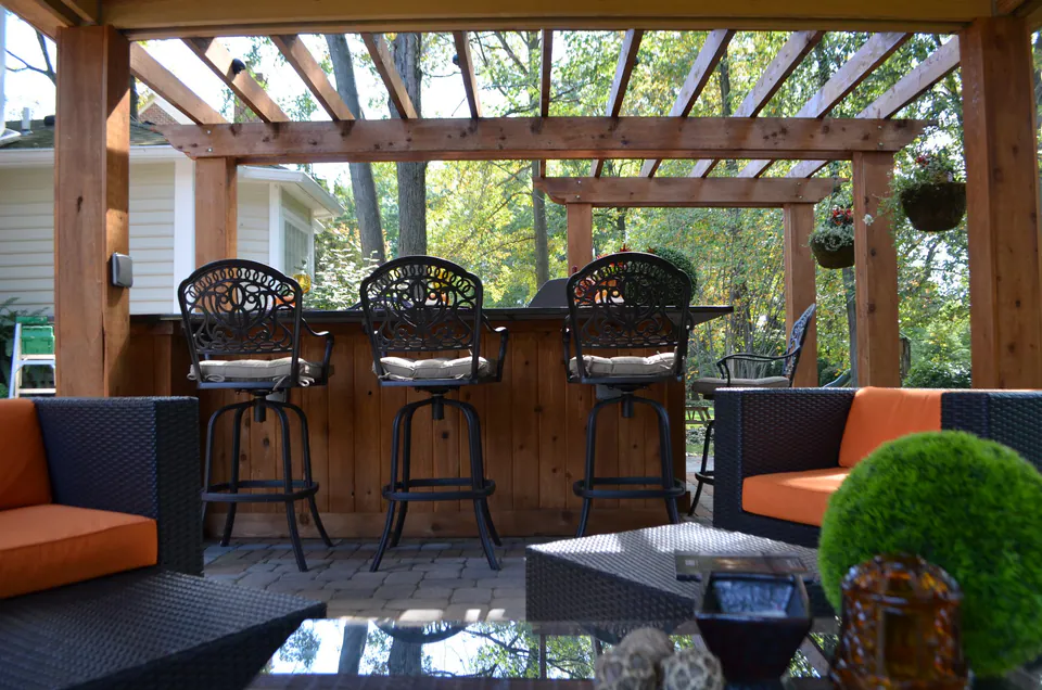 Cedar bar counter with swivel stools under a cedar pergola, with lounge seating in front